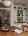  single-family home’s remodeled kitchen with a kitchen island with a reclaimed, myrtle wood butcher block counter top. Behind the island is a bank of built-in cabinet, and a hall way leading to the home’s entry and mudroom.