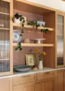 A built-in storage hutch in a remodeled single-family home, featuring white oak casework with shaker cabinets and drawers, a white quartzite countertop, flanking cabinets set with reeded glass panels, and central open shelving backed by a rusty red, penny tile backsplash.