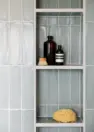 A close-up view of a niche in a sea-foam-green-tiled shower. Stored on the niche are bottles of soap and shampoo, a sponge, and a scrub brush.