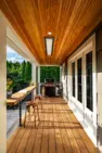 The covered porch of this modern backyard remodel, connected to a home in a traditional style. The deck has bar seating and a bar overlooking the rest of the yard, a grill at the back, and an overhead heater.