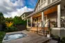 An updated, modern backyard showing a Kebony deck with an in-ground hot tub. The hot tub is running with its jets on.