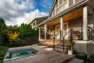An updated, modern backyard showing its Kebony deck with an in-ground hot tub. The hot tub is off and its cover is being shown stowed under the deck's built-in bench seat.