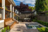 An updated backyard space in a modern design, with a covered porch with a staircase to a lower deck. The deck has an in-ground hot tub. Beyond the deck, outdoor furniture can be seen.