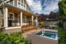 Overall view of a small backyard with a Kebony deck with an in-ground hot tub, a porch at the house, and a patio beyond the deck.
