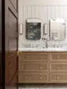 A custom white oak vanity sits beneath a marble counter and backsplash, between brass sconces and curved mirrors, on a marble mosaic floor. - Tangletown Craftsman – Interior Design for a Craftsman Home – Board & Vellum
